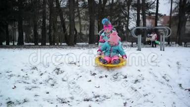 年长的姐姐帮助小婴儿滑下山。 两个女孩享受雪天气和雪橇。