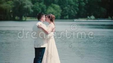结婚纪念日。 美丽的一对夫妇享受他们的幸福，站在码头上，拥抱和亲吻。 结婚礼服，花束