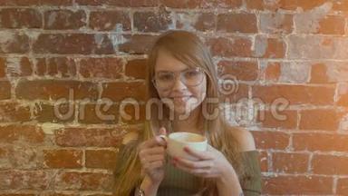 美丽的年轻微笑的女人，<strong>端着</strong>一杯热咖啡站在砖墙旁边