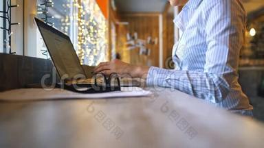一张侧面照片拍摄的是一位年轻漂亮女子坐在咖啡厅的木桌旁忙着操作笔记本电脑的手