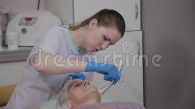 专业美容师在美容办公室为一名携带微<strong>电流</strong>的老年妇女执行手术。