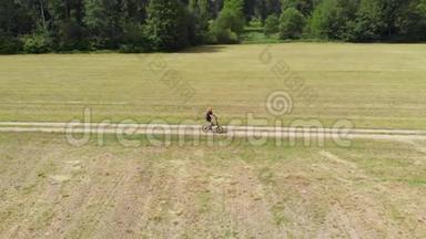 空中：男子骑自行车沿着乡间小路穿过耕地和农田，阳光明媚的一天，环保的交通运输
