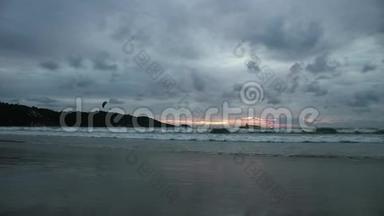 日落时的海景倒映在潮湿的沙滩上，海浪涌来。 有伞的摩托艇
