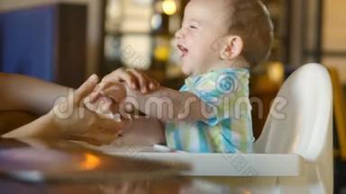 妈妈用嘴和手擦着可爱的宝宝。 一个迷人的孩子笑着拍手。 4k.