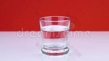 一片泡腾的止痛片落入玻璃杯中，在红色背景下溶解慢镜头的阿司匹林