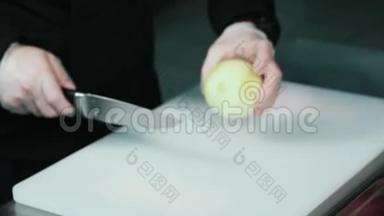 手拿洋葱。 厨师在白色切割板上切洋葱特写。 在餐厅厨房做饭。 双手放着
