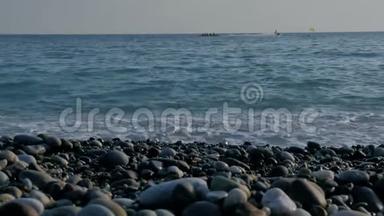 人们坐在海上的充气香蕉上。 带有泡沫的大透明波。 海卵石滩，五颜六色的石头。