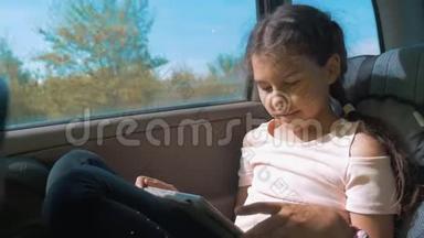 小女孩坐在车里，带着平板电脑，互联网，社交媒体去旅行。 汽车概念旅行运输运动