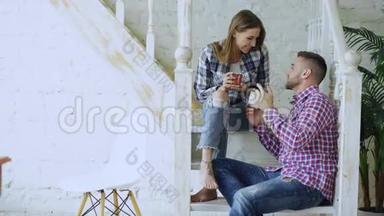年轻、快乐、可爱的一对夫妇在家中坐在楼梯上喝茶聊天