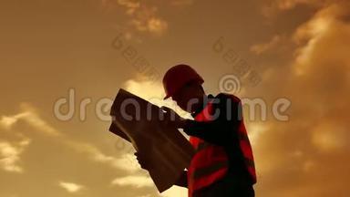 工人剪影工人建设者男子与红色头盔和牛仔裤衬衫附近的工业墙。 剪影工人生活方式