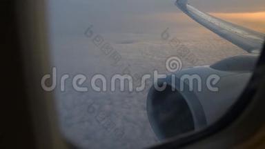 飞机机翼通过飞机窗口的视图。 日出时在云层上方飞行。
