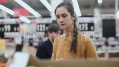 年轻女人在<strong>超市</strong>里选择绿色苹果的正面景色。 年轻女孩考虑<strong>水果</strong>。 4K