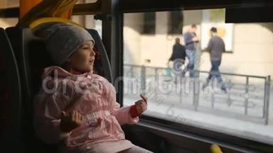 小金发女孩穿着粉红色的夹克，孩子坐在公共汽车车厢里。 坐在她的座位上<strong>看</strong>着<strong>玻璃</strong>