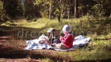 可爱的小男孩秋天在森林里野餐，坐在草地上，在户外吃饭。 侧视。