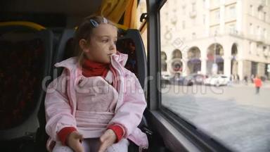 小金发女孩穿着粉红色的夹克，孩子坐在公共汽车车厢里。 坐在她的座位上看着玻璃