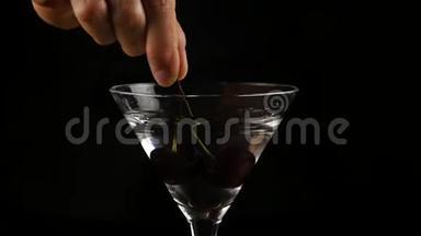 樱桃被扔进一个杯子里，酒精鸡尾酒在黑暗的背景下。 准备鸡尾酒和派对概念。 慢慢慢慢
