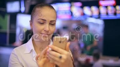 一个年轻的女人坐在快餐店里，拍自拍，在智能<strong>手机屏</strong>幕上看她的照片。