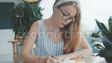 年轻的金发女人做白日梦，在她的日记里写日记。 女人在咖啡馆的笔记本上写字。