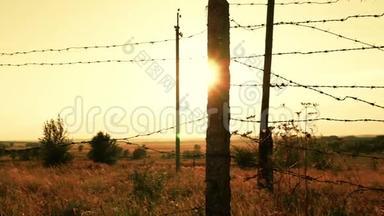 日落特写时用带刺铁丝网的监狱或军事围栏。 边界区、危险区、安全区、军事围栏