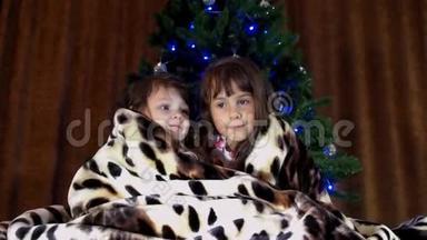 孩子们坐在圣诞树附近的地毯下。 两个小<strong>女孩</strong>被一条<strong>斑点</strong>毯子覆盖着。 两个姐妹玩游戏