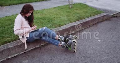 开朗的年轻女孩坐在街上，使用平板电脑触摸屏。 女孩穿着<strong>粉色</strong>背心，<strong>蓝</strong>色牛仔裤