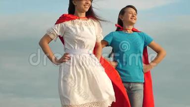 两个穿着超级英雄红色<strong>斗篷</strong>的女孩站在蓝天上，风吹着<strong>斗篷</strong>。 妈妈和女儿玩
