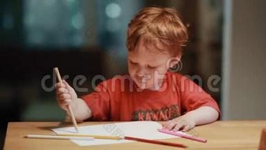 一个可爱的小男孩坐在桌子旁，用白纸上的彩色铅笔画画。