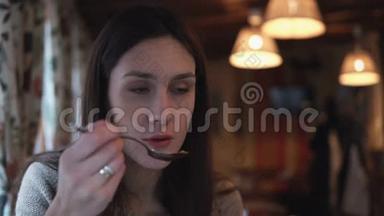 年轻迷人的黑发女人坐在咖啡馆里，用勺子说话和吃饭。 一个女孩在和别人谈话
