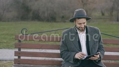 Hipser创意商业人士戴着帽子，使用平板电脑，休息时坐在公园的城市街凳上