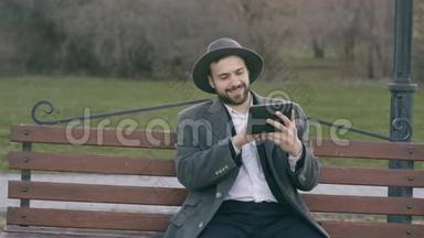 Hipser创意商业人士戴着帽子，使用平板电脑，休息时坐在公园的城市街凳上