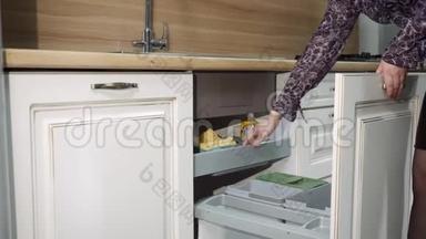 女孩打开水槽下面的抽屉，展示着厨房橱柜的填充。 经典的厨房布景。