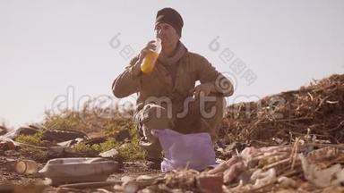 一个肮脏的无家可归的饥饿男人在垃圾堆里喝着包裹里丢失的果汁，步行<strong>去寻找</strong>