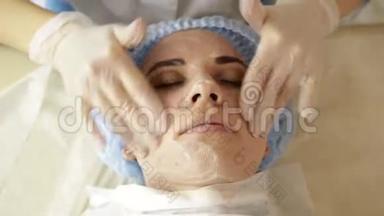 美丽的女人在水疗沙龙接受美容治疗。 美容医生戴着医用手套，摸着女孩`脸。