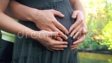 双手抚摸怀孕的肚子。 丈夫`手抚摸着怀孕妻子的腹部。 柔和的夕阳照亮了