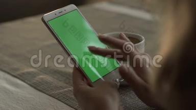 女人在背景咖啡杯上用绿色屏幕手机打字