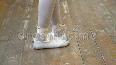 在芭蕾训练期间，<strong>一个</strong>穿白色芭蕾舞鞋的女孩`在<strong>一个</strong>旧木<strong>地板上</strong>的腿特写。 古典元素