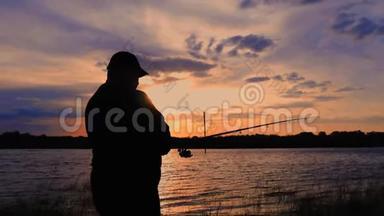剪影渔夫在背景黄昏日落时在河中投掷鱼竿。 钓鱼时傍晚美丽的日落