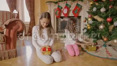 两个穿着睡衣的<strong>活泼</strong>女孩坐在圣诞树下，打开盒子拿礼物