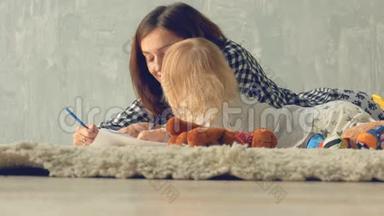 母女女孩用铅笔画一幅画。 妈妈拥抱和亲吻宝贝。