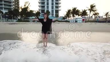 穿着黑色衣服的女人站在<strong>波浪</strong>状的海<strong>水中</strong>，在阳光明媚的艾尔斯海滩上迈阿密度假胜地附近送空气亲吻