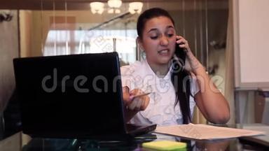 一个漂亮的年轻商务女孩坐在一张桌子旁的办公室里用手机谈论一个商务项目