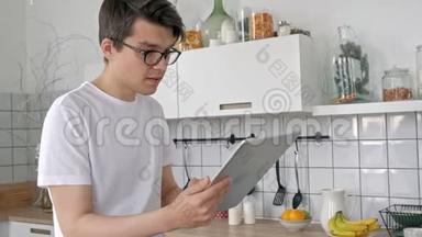 <strong>家中</strong>有魅力的男人在厨房里用平板电脑发送信息，社交媒体微笑着享受现代生活方式