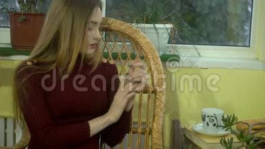 可爱的年轻女孩，美丽的化妆，坐在柳条椅子上，喝热咖啡，看着窗外，下雪