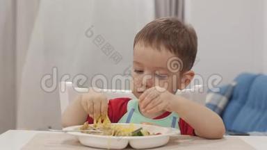 小孩子坐在围兜里的一张桌子旁吃自己的意大利面，可爱的宝宝心甘情愿地吃。 可爱的小宝宝
