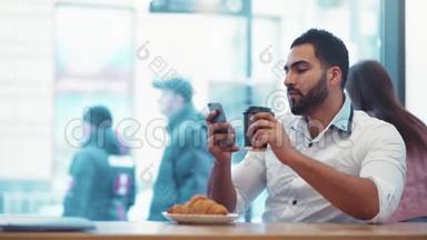英俊的男人喝着一杯咖啡，微笑着走向手机屏幕。 <strong>日常生活</strong>，社交网络。 使用
