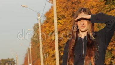 一个头戴帽子的女孩，头发松松的站着，手举起来，搭便车。 秋天的森林和