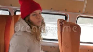 年轻开朗的女人戴着红帽子，在一个悲伤的日子乘公共汽车旅行。 她听音乐
