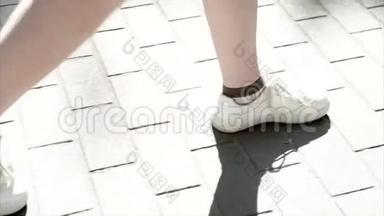 穿着白色运动鞋的女人独自向前走。 在沥青上台阶。