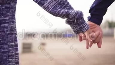 海滩上一对年轻夫妇牵着手一起散步的特写镜头。 慢镜头
