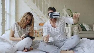 一对年轻可爱的夫妇，带着平板电脑和虚拟现实耳机，坐在床上<strong>玩</strong>360<strong>VR</strong>电子游戏